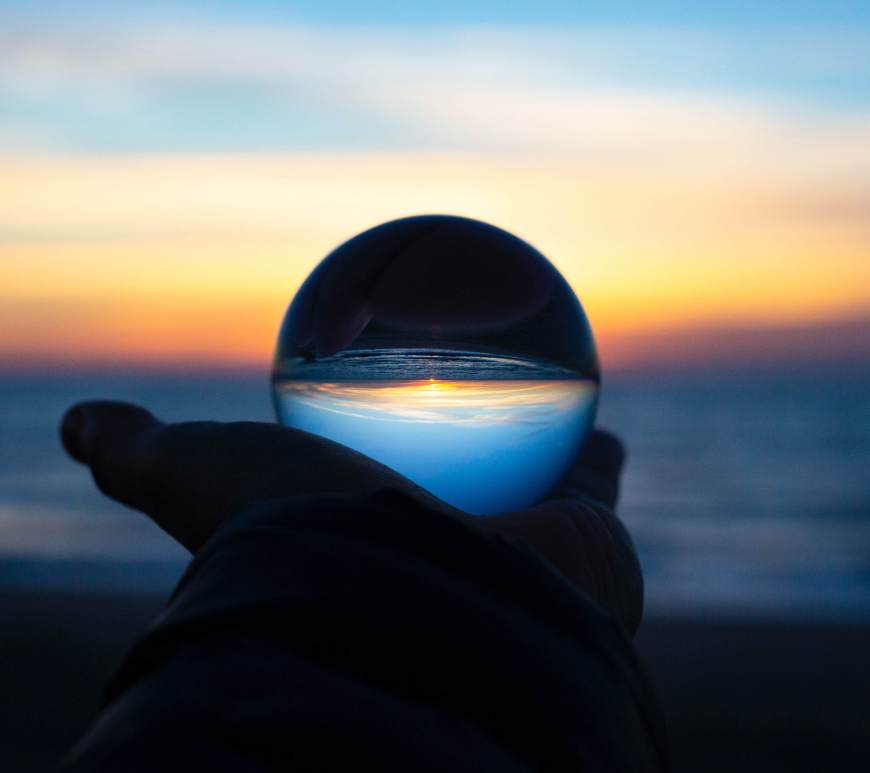 A hand holding a crystal ball by a beach
